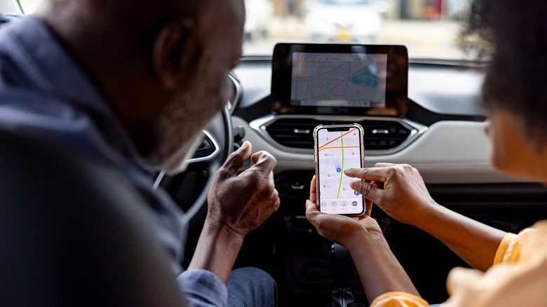 Senior black couple in a car using a mobile phone for navigation