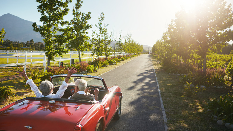 Gray-haired couple riding in a red convertible on a sunny day