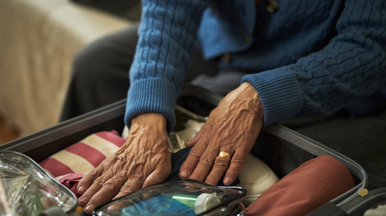 Closeup of sweater-clad old person packing a suitcase
