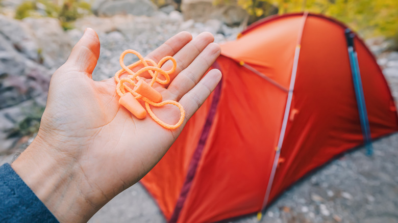 Earplugs in the hand of a hiker, held in front of an orange tent