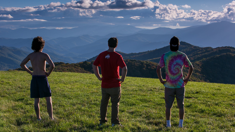 Three male hikers peer at the distant Tennessee horizon viewed from Max Patch along the Appalachian Trail