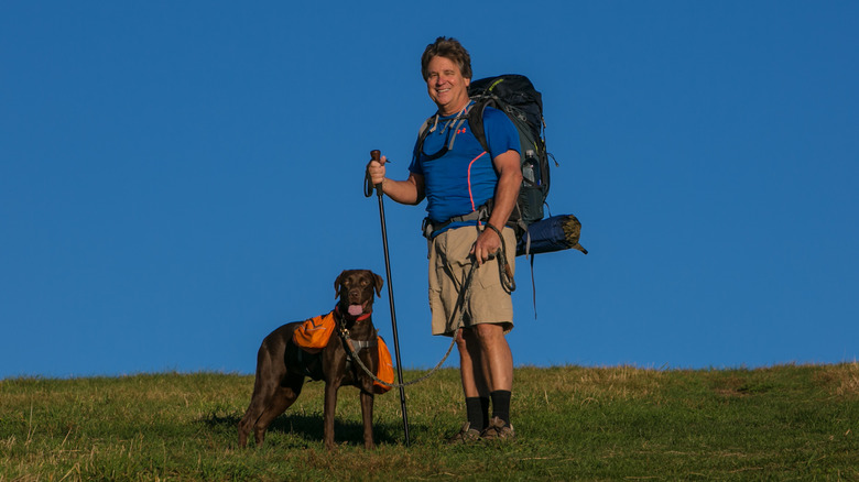 A long-distance hiker on the Appalachian Trail at Max Patch with his dog, which wears a hi-vis vest