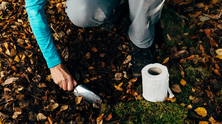 A female hiker prepares a toilet hole on the ground with toilet paper and a trowel