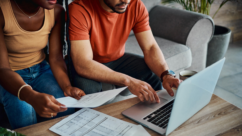 Two people sit next to a computer with paperwork