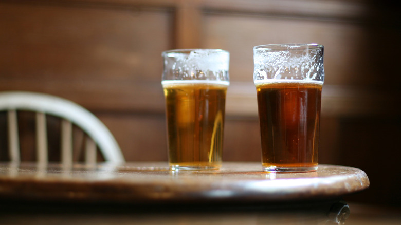 Two pints of ale sitting on a British pub table in a traditional setting