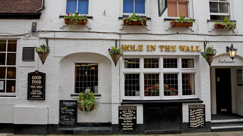 Front view of a popular British gastropub called The Hole In The Wall housed in a historic white building with gold and black signs