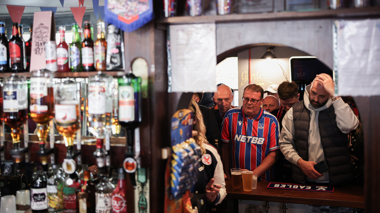 Fans queue for a drink in a busy local pub during a football match