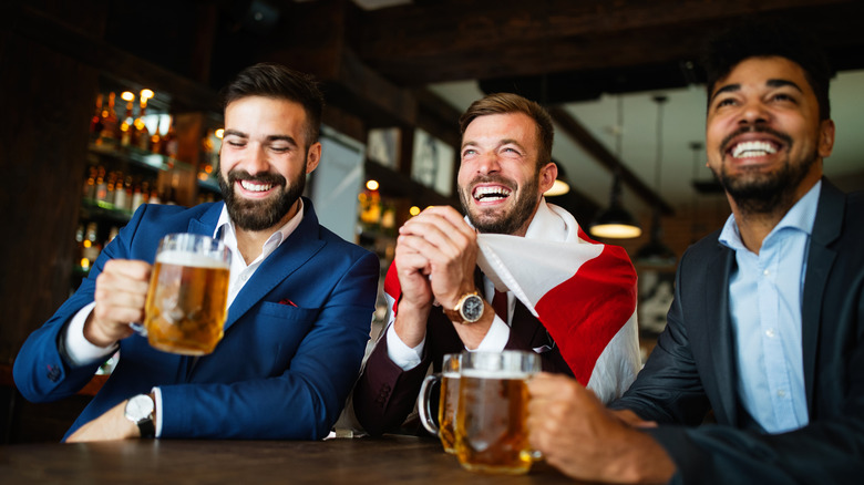 Group of friends at the pub watching football game and drinking a round of beer