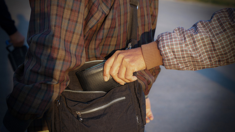 close up image of someone stealing a wallet from a bag a man is carrying as he walks down a street.
