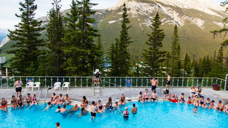 Summer visitors soaking in the historic hot, mineral-rich water of Banff Upper Hot Springs with Rundle and Cascade Mountains in the background