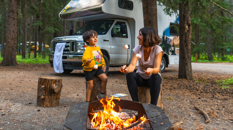 A mother and son roast marshmallows over a campfire next to their camper van at Banff National Park