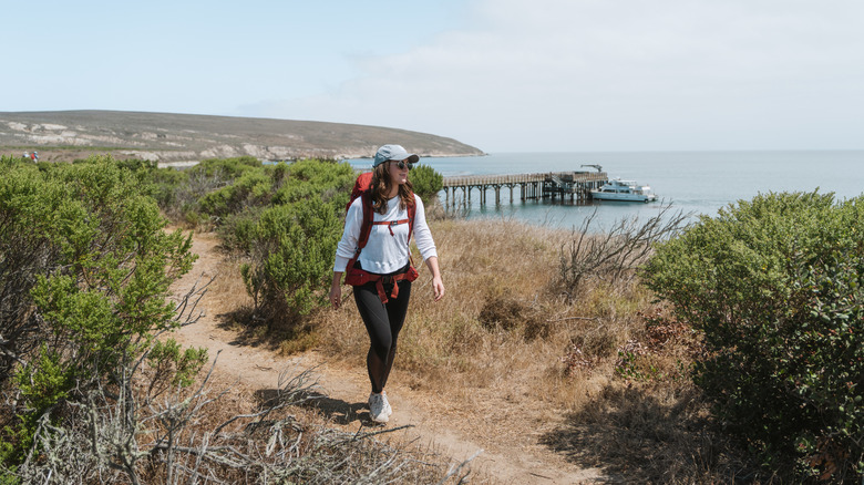 A woman hikes along a trail wearing sunglasses, a hat, and a long-sleeved shirt on Santa Rosa Island in Channel Islands National Park