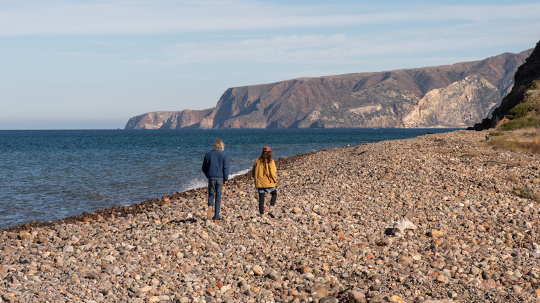 A man and a woman walk down a rocky beach in the Channel Islands, California while waiting for their ferry to arrive