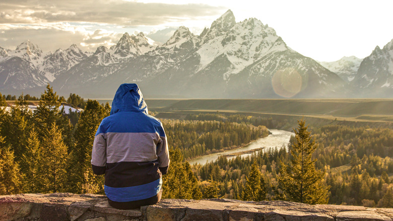 A person wearing a jacket sits on a wall looking at mountains in Grant Teton National Park