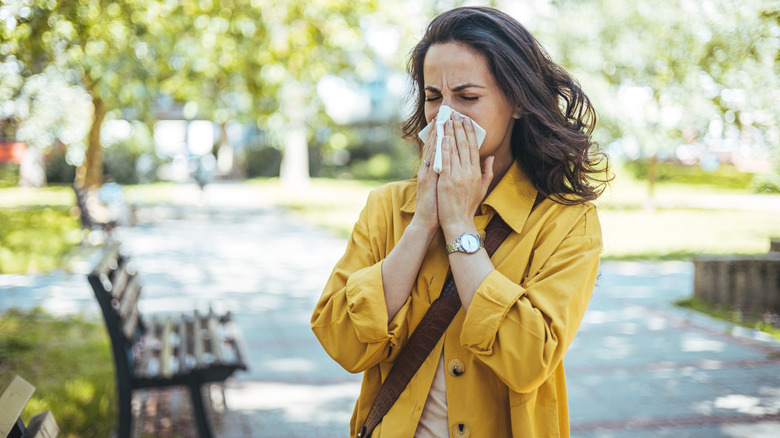 Woman blowing her nose while walking through a park