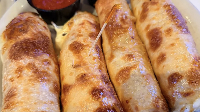 Close-up view of Kilroy's famous stuffed breadsticks with cup of marinara sauce in background
