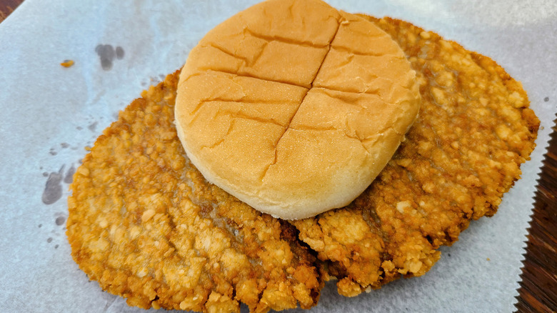 Comically oversized pork tenderloin sandwich extending far past bun, sitting on parchment paper, top view