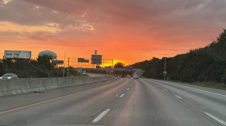 View through a car windshield of a beautiful orange sunset and cars driving on I-465 in Indianapolis, IN