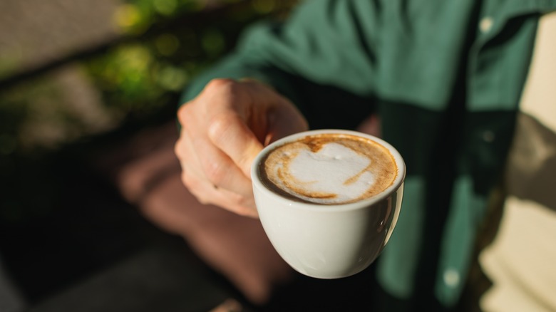 A man's hands holding a foamy cappuccino