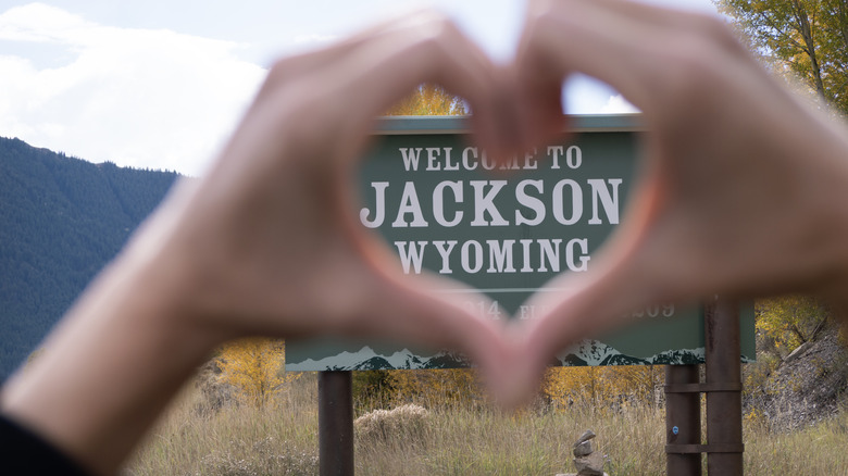 A person makes a heart out of their fingers in front of the Jackson, Wyoming, welcome sign