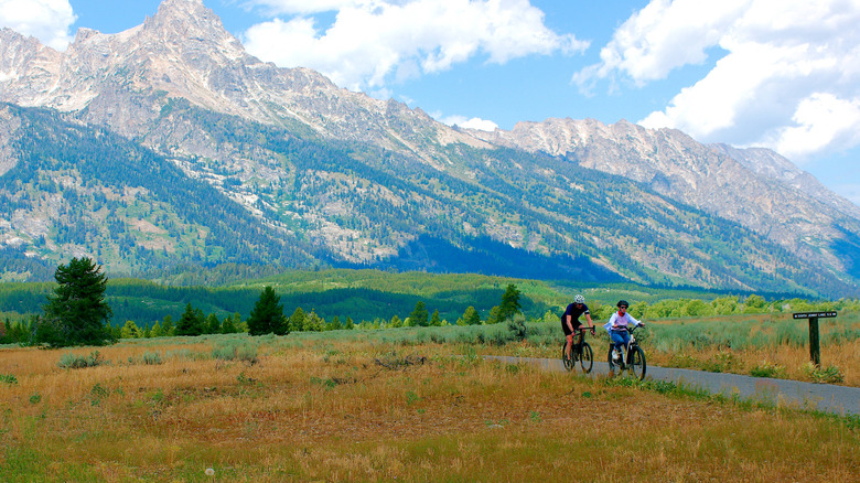 A pair of bicyclists traveling on the bike trail running along the Grand Teton Mountain Range