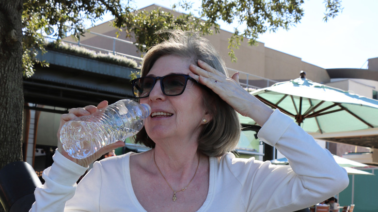 Woman drinking water while wiping sweat from her face