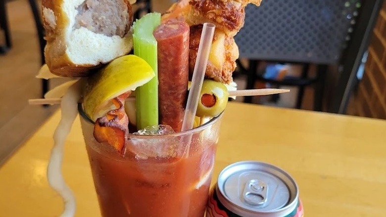 A bloody mary with elaborate garnishes including sausage stick, olives, celery, bacon, and a brat in a bun at West Allis Cheese and Sausage Shoppe