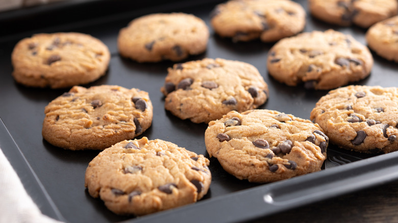 Homemade chocolate chip cookies cooling on a black baking tray