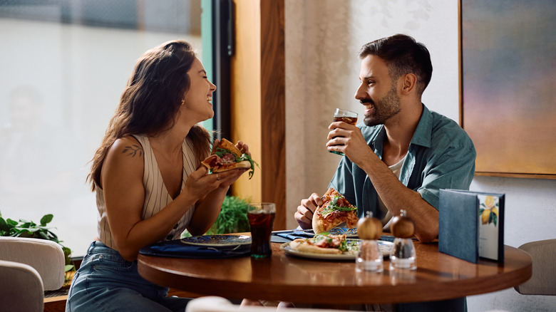 A young couple eats pizza at a restaurant table