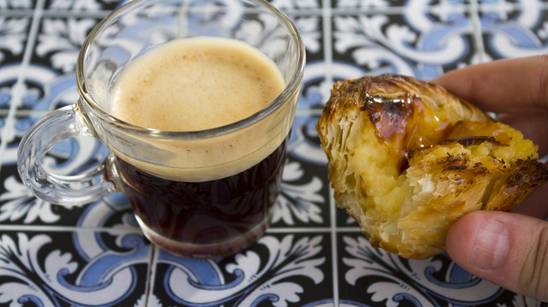 Hand holding a Portuguese pastel de nata, with black espresso coffee