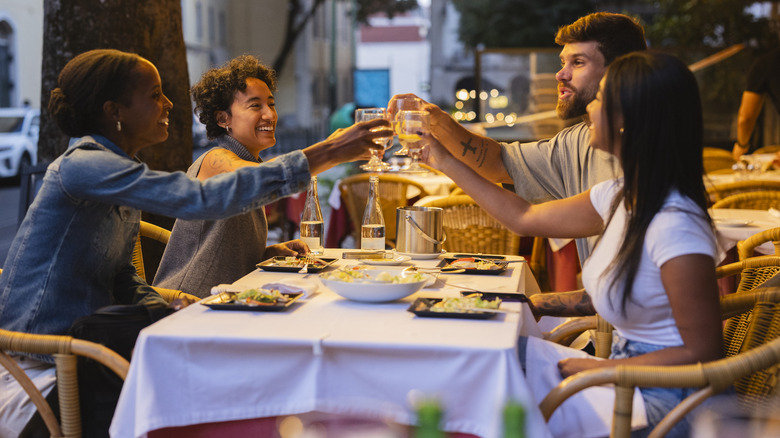 Four joyful friends are toasting drinks while sitting at a table in Lisbon