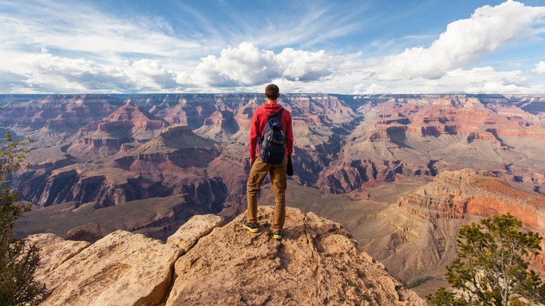 A hiker with a small backpack stands on the cliff edge at Grand Canyon National Park
