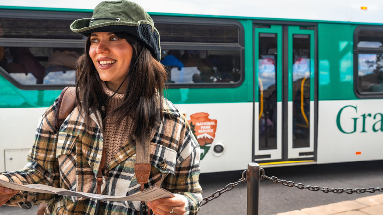 A smiling woman stands in front of a Grand Canyon shuttle bus with a map