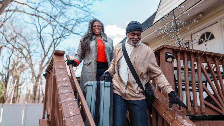 An couple carry luggage down a flight of stairs at a house