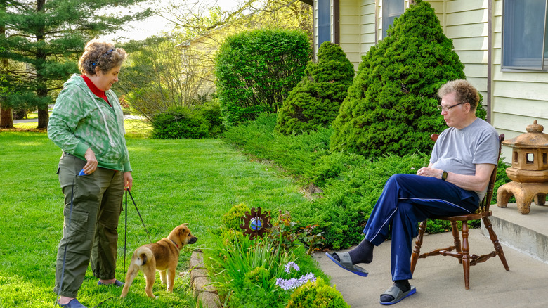 A woman with a small dog visits a man at a suburban house