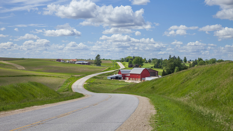 A road winds through the Iowa rural countryside on a sunny day, past a bright red barn