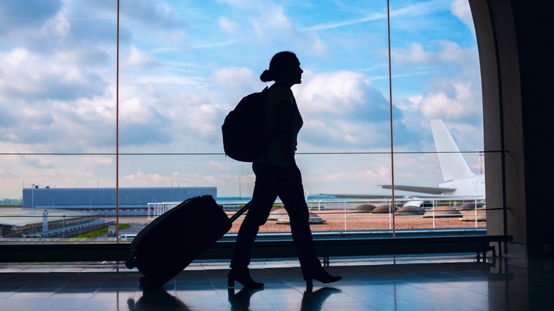 Silhouette of passenger walking in front of glass wall at airport