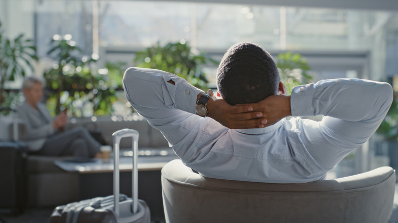 From behind, a person relaxing with arms outstretched in lounge.