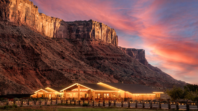 Exterior view of Red Cliffs Lodge Moab, near Moab, Utah, lit up around sunset, with sandstone cliffs visible in the background
