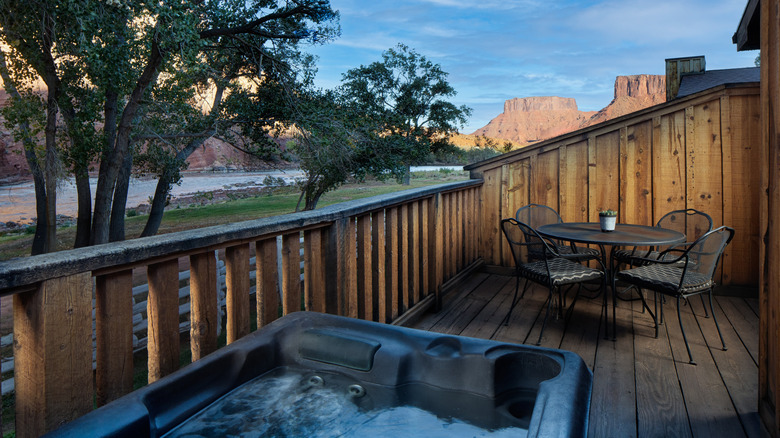 View from the outdoor deck of the Riverside King Cabin at Red Cliffs Lodge Moab near Moab, Utah, featuring an outdoor hot tub and dining area, with trees and the Colorado River in the background