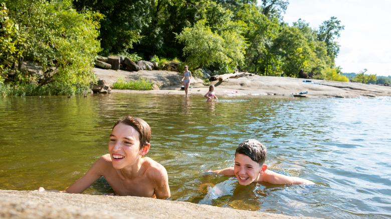 Two boys swimming in a river with others getting into the river in the background