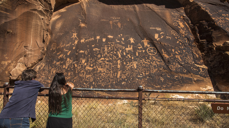 Two visitors admiring the sandstone carvings at Newspaper Rock.