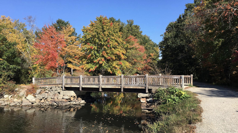 A wooden bridge crossing over a section of the Blackstone River on an autumn day in Blackstone River and Canal Heritage State Park in Uxbridge, MA