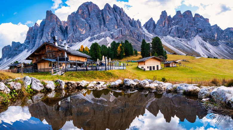 View of Geisleralm, a small alpine hut with mountains and a pond surrounding in Val Di Funes, Italy.
