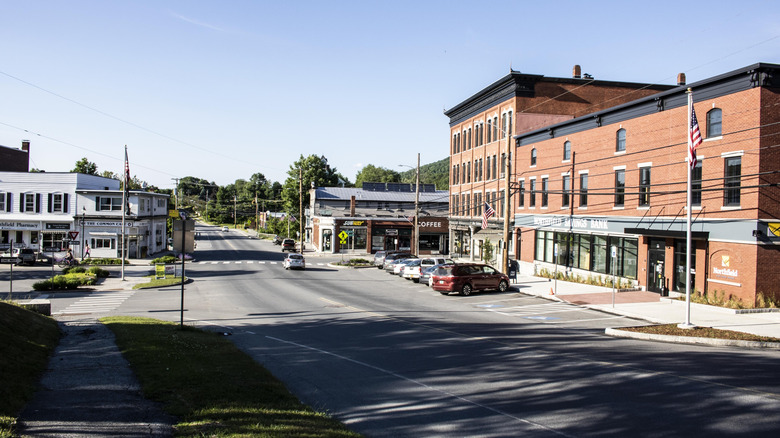 Several brick storefronts line a downtown street on a sunny summer day in Northfield, Vermont