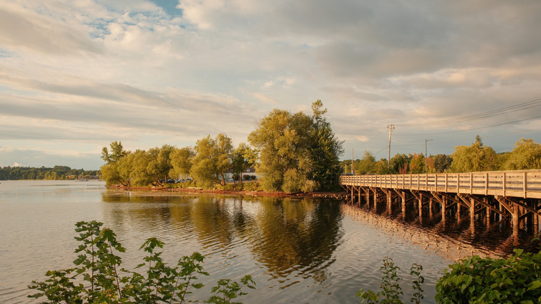 A golden sun illuminates trees, water, and a wooden bridge on Lake Memphremagog in Vermont
