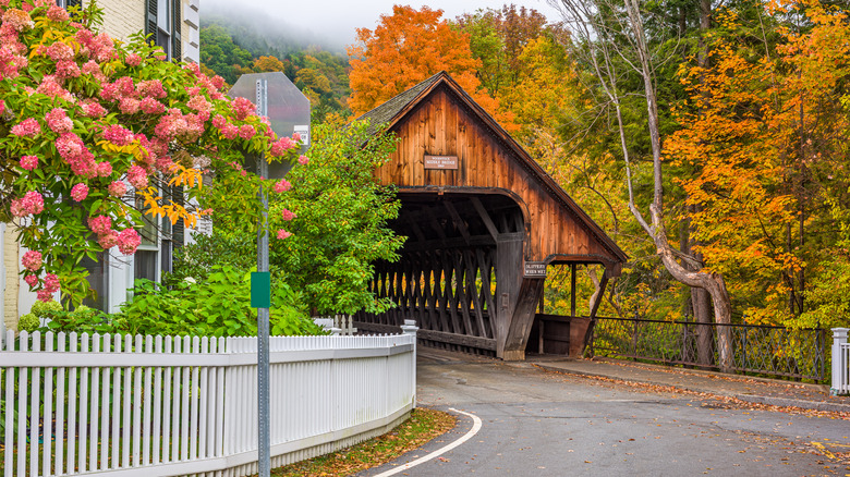 Flowers and fall foliage on a street leading to the entrance of Middle Covered Bridge in Woodstock, Vermont