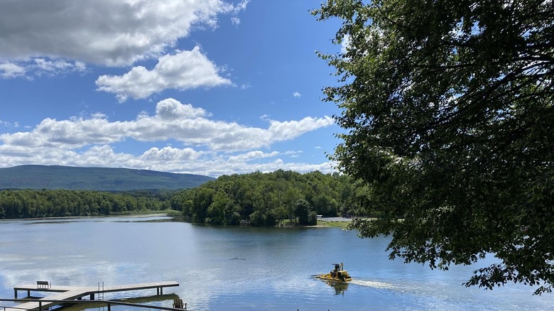 A lone boater travels across Lake Paran near a small dock on the water, which reflects the sky above, under partly cloudy skies