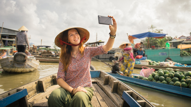 Woman tourist taking a selfie onboard a floating market boat
