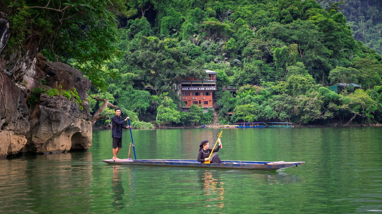 Locals dressed in black clothes on a narrow wooden boat against karst mountains and forests